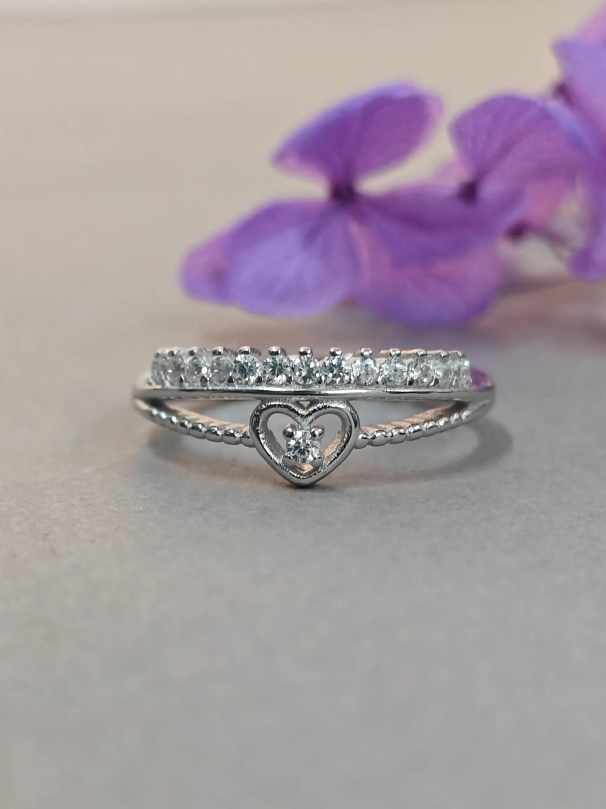 Silver ring with heart design on a light background with purple flowers